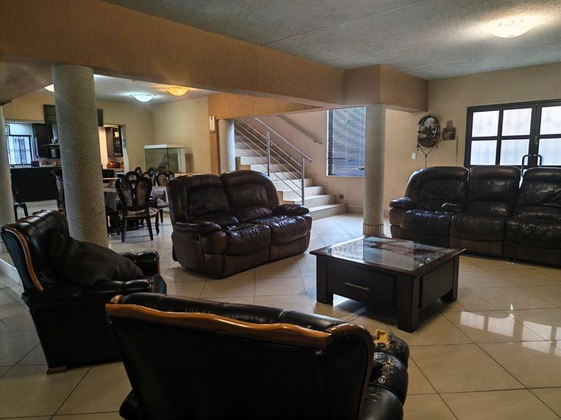 Spacious open-plan living area featuring structural columns, tiled flooring, and a staircase with a modern metal railing, offering a versatile layout for family living.