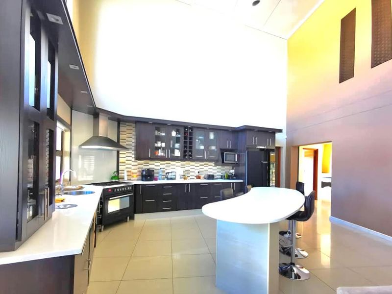 Spacious modern kitchen featuring dark cabinetry, stone countertops, a central island, and impressive double-height ceilings with integrated appliances.