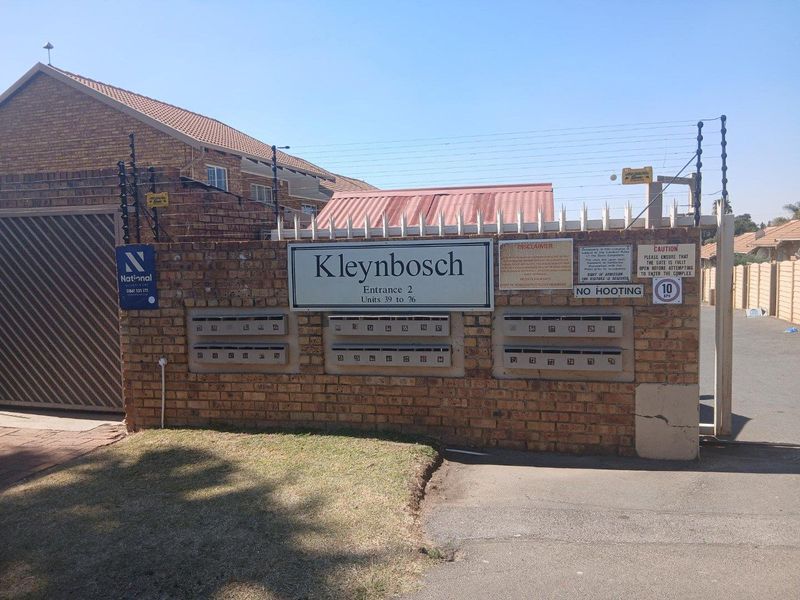 Front entrance view of Kleynbosch townhouse complex featuring a brick boundary wall, integrated mailboxes, and security fencing.