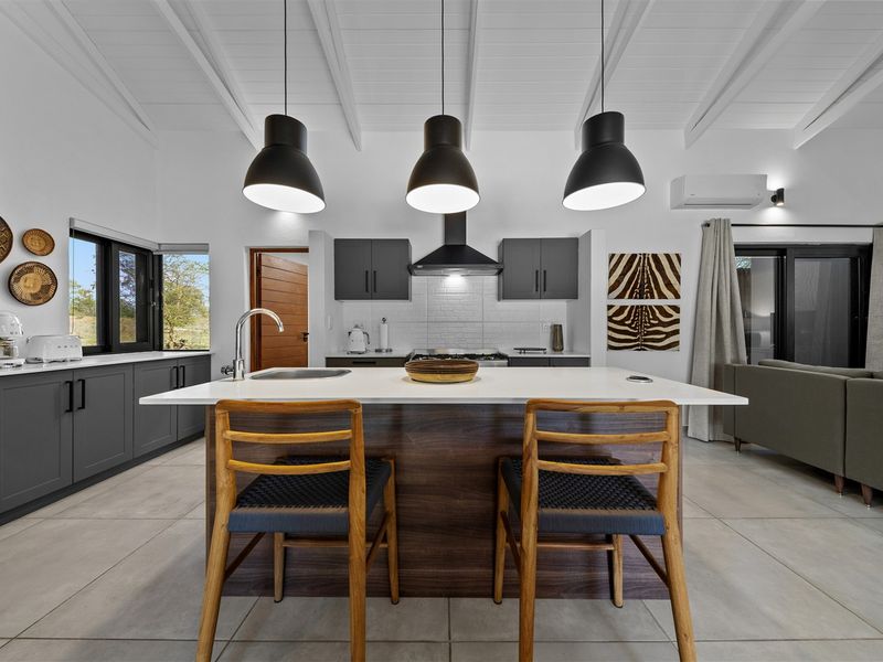 Modern open-plan kitchen featuring a central island with sink, dark cabinetry, high-quality finishes, and exposed beam ceilings in a bright, contemporary living space.
