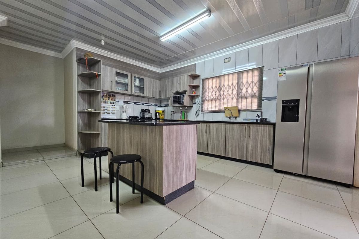 Modern kitchen featuring wood-grain cabinetry, granite countertops, a central island with seating, and large format floor tiles.