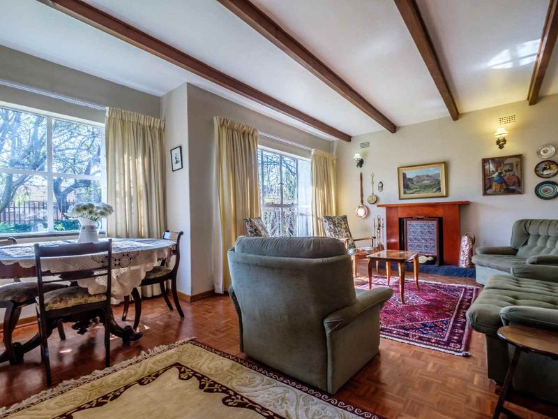 Spacious living room featuring classic parquet flooring, exposed timber ceiling beams, and a traditional fireplace with a timber mantel.