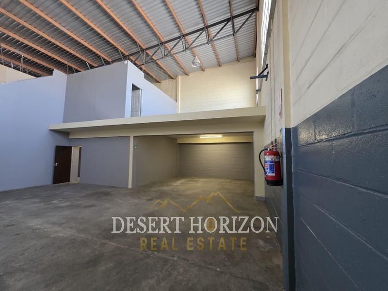 Spacious industrial utility area featuring a mezzanine level, exposed steel roof trusses, and durable concrete flooring, suitable for storage or workshop operations.