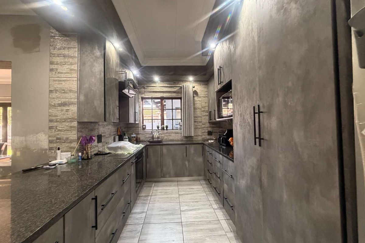 Modern kitchen featuring dark textured cabinetry, granite countertops, integrated appliances, and recessed lighting, with some minor wall finishing required.