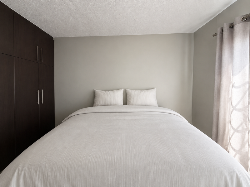 A well-maintained bedroom featuring dark built-in cupboards and neutral wall tones, providing a clean and functional sleeping space.