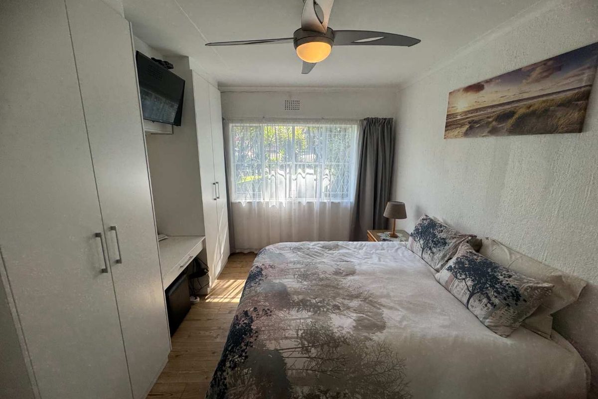 A functional bedroom featuring built-in floor-to-ceiling wardrobes, a integrated desk area, and a ceiling fan.