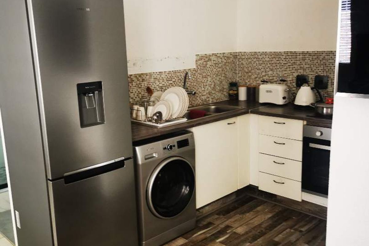 Compact kitchen featuring wood-look flooring, mosaic tile backsplash, built-in oven, and integrated cabinetry with space for laundry appliances.