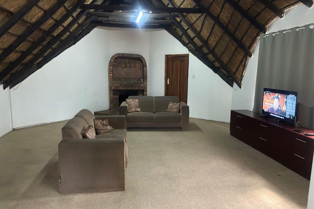 Spacious living area featuring a high vaulted thatch ceiling, exposed brick fireplace, and neutral carpeting, offering a rustic and open atmosphere.