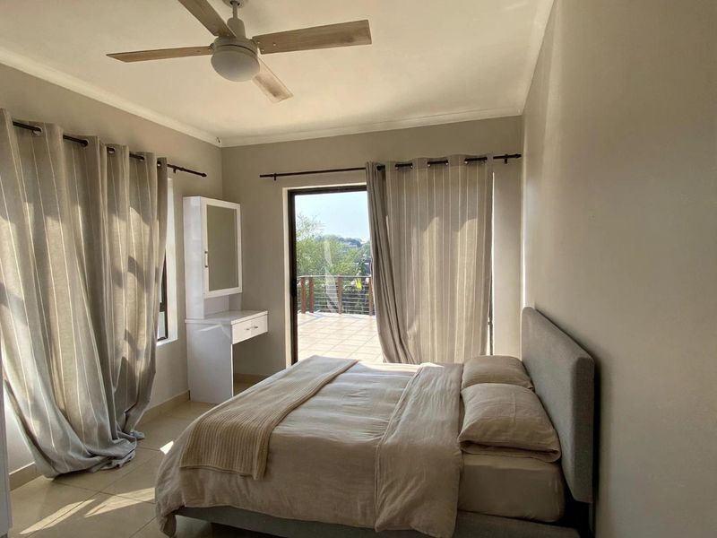 A bright bedroom featuring tiled flooring, a ceiling fan, and direct access to an outdoor balcony through sliding glass doors.