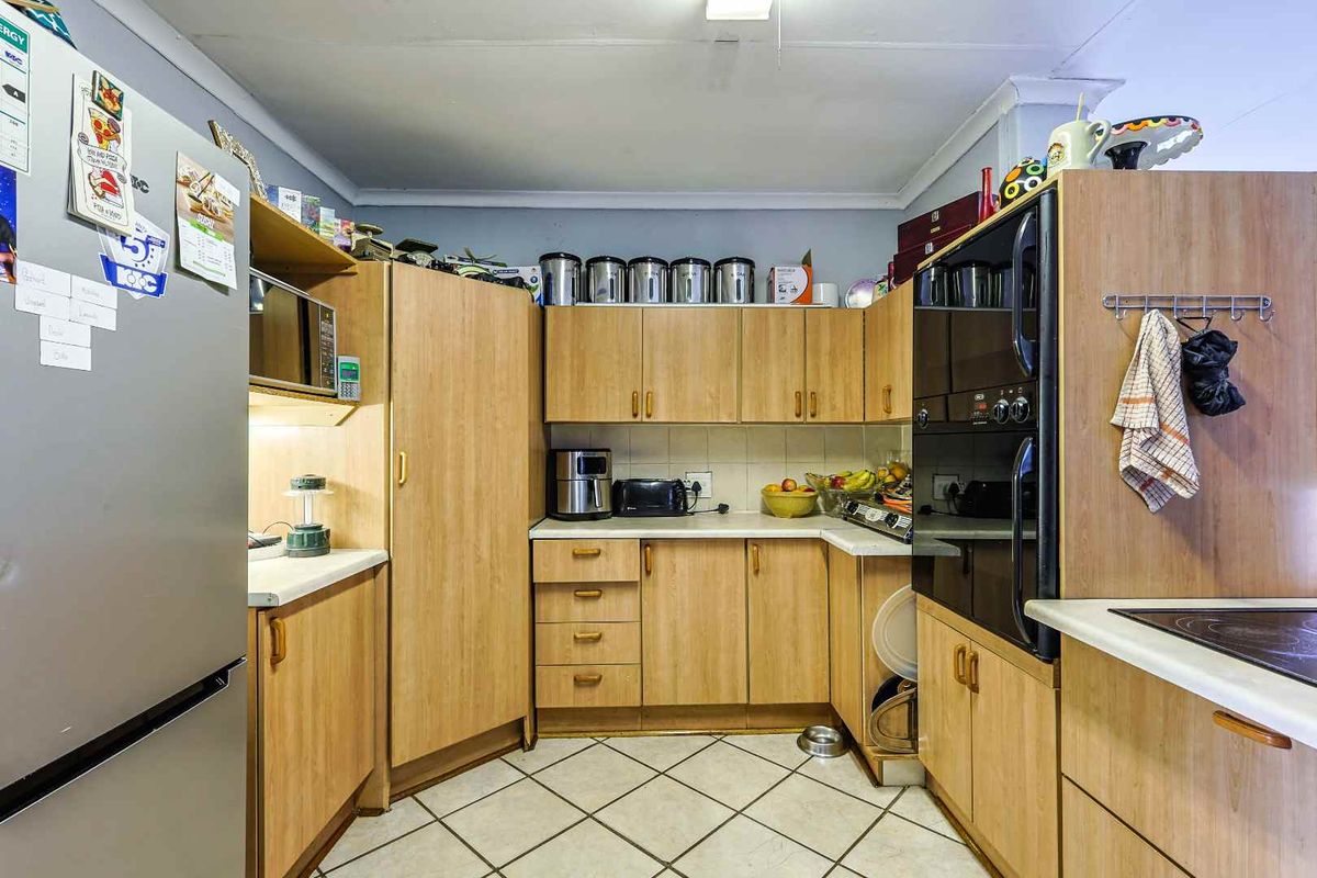 A functional kitchen featuring light wood-finish cabinetry, tiled flooring, and built-in oven and hob appliances.