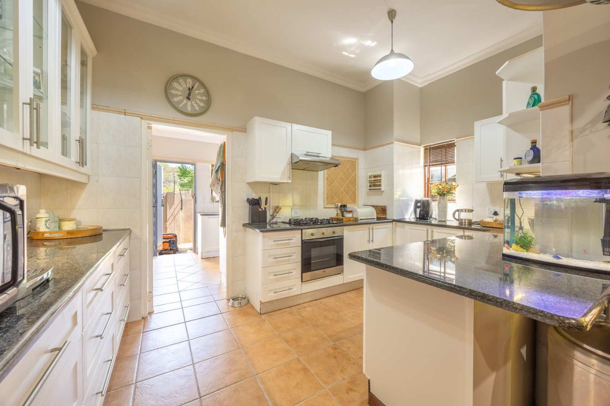 A well-maintained kitchen featuring granite countertops, white cabinetry, built-in oven with gas hob, and tiled flooring, with an adjacent doorway leading to a utility area.
