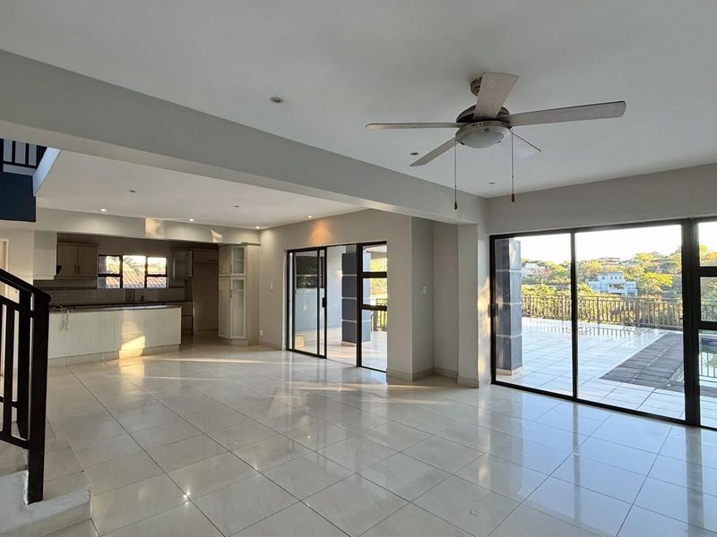 Spacious open-plan living area featuring tiled floors, a ceiling fan, and large sliding doors leading to an outdoor patio and pool area.