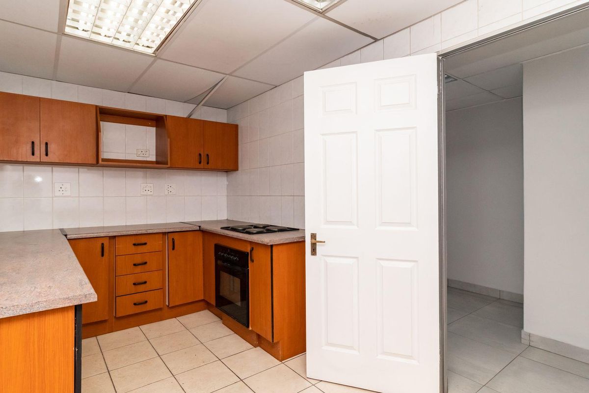 A functional office kitchenette featuring wooden cabinetry, built-in oven and hob, tiled flooring, and a suspended ceiling with integrated lighting.