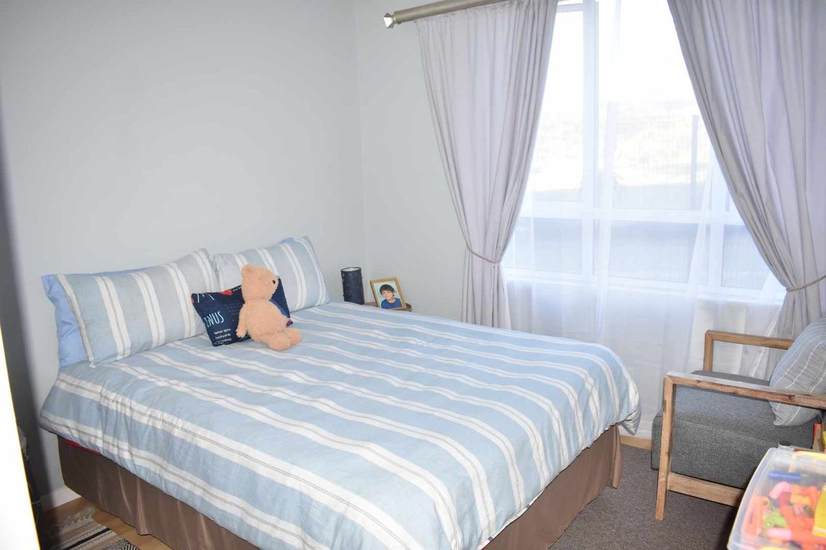 A cozy bedroom featuring neutral wall finishes, carpeted flooring, and a large window with curtain fixtures.