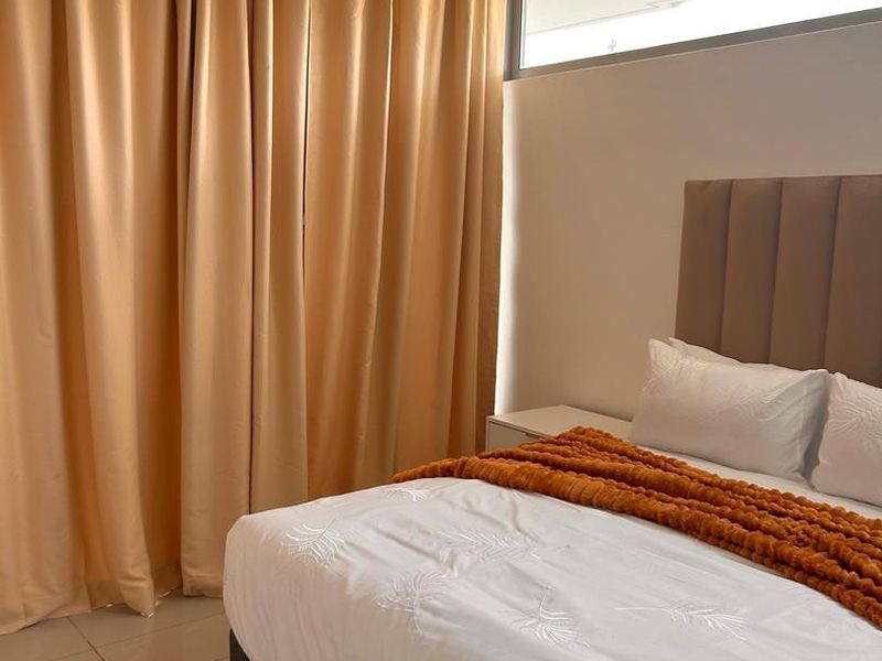 A well-maintained bedroom featuring neutral tiled flooring, a high-level clerestory window for natural light, and full-length curtains.