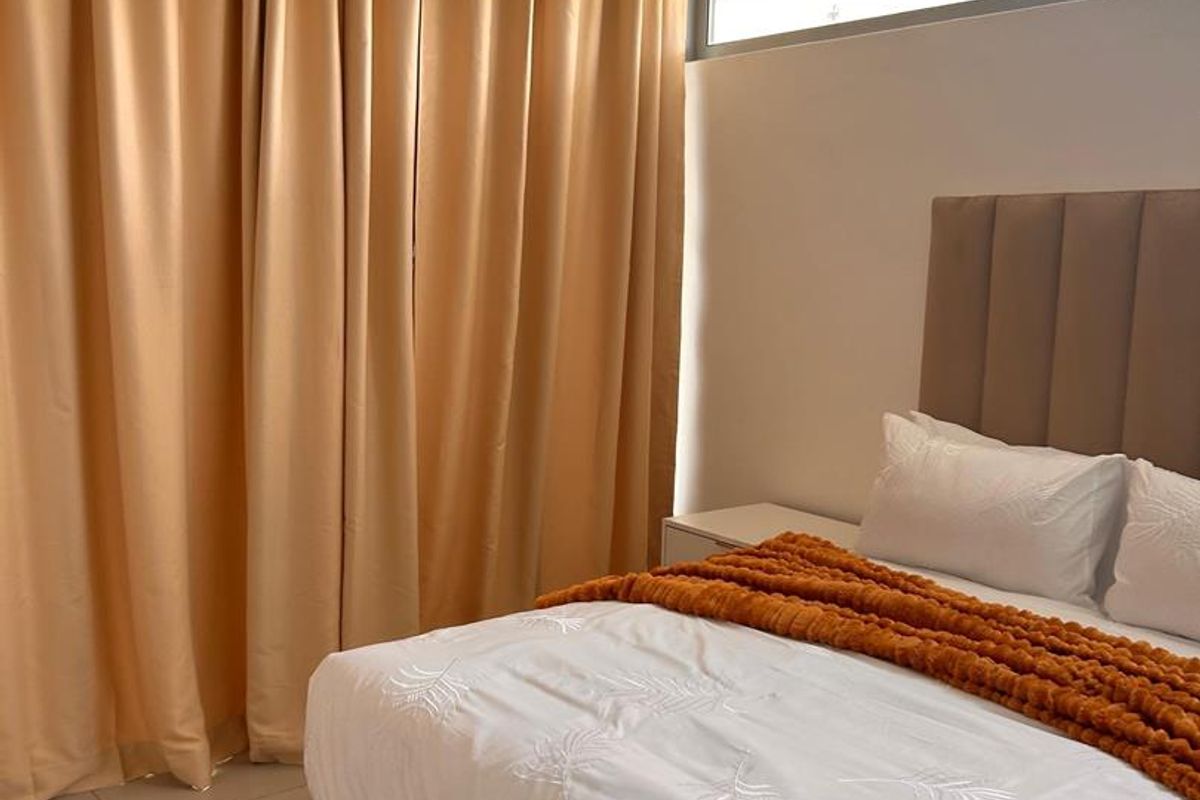 A well-maintained bedroom featuring neutral tiled flooring, a high-level clerestory window for natural light, and full-length curtains.