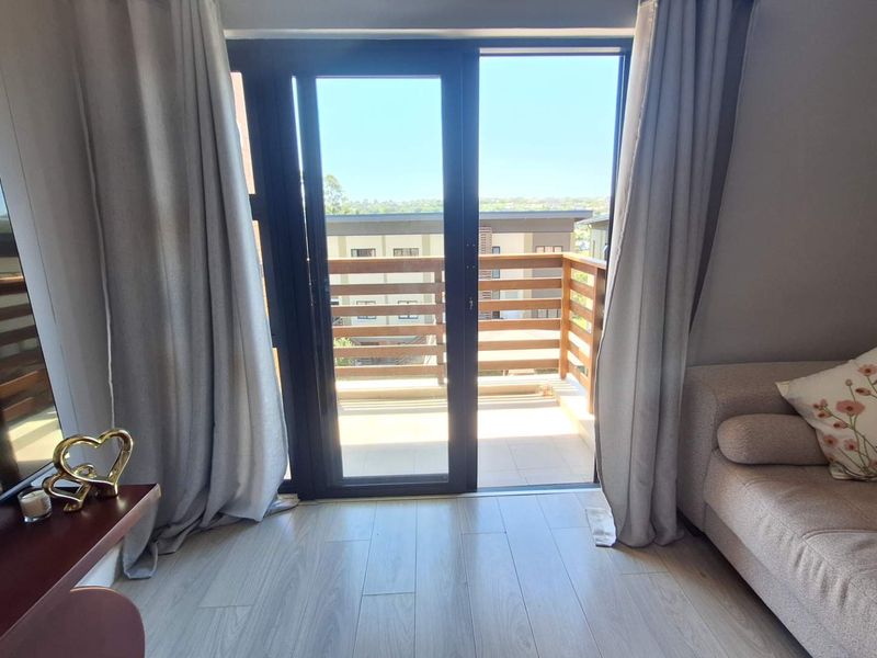 A bright living room featuring modern tiled flooring and a sliding glass door that opens onto a private balcony with a wooden railing.