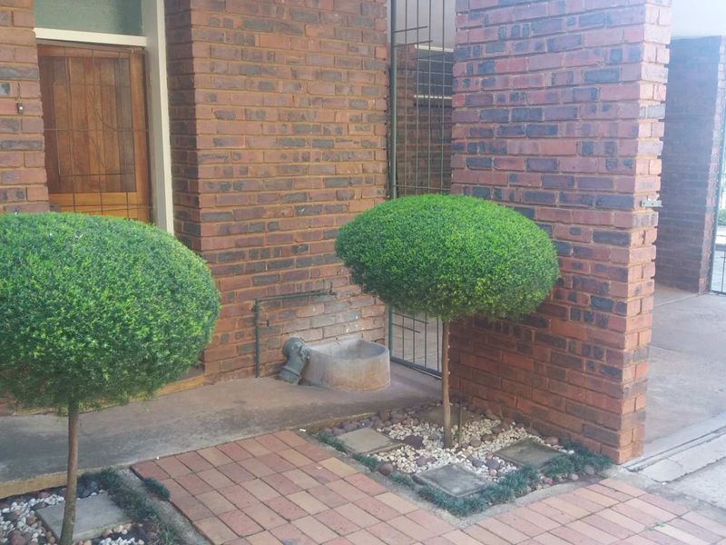 Front entrance area of the townhouse featuring a classic brick facade, timber door, and paved walkway with established landscaping.