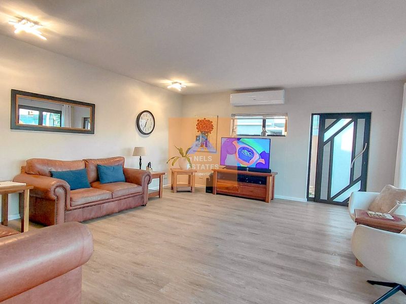 Spacious living room featuring light-toned laminate flooring, air conditioning, and a modern glass-paneled entrance door with access to the patio.
