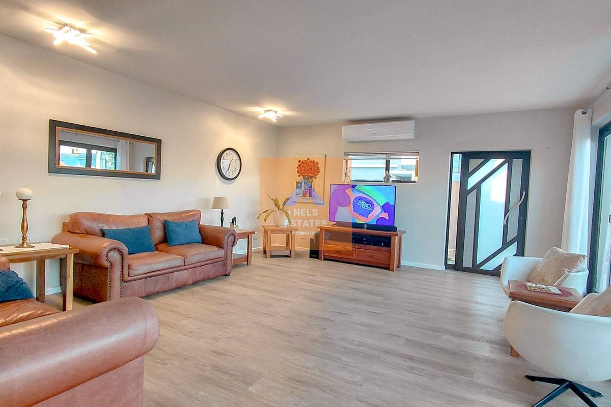 Spacious living room featuring light-toned laminate flooring, air conditioning, and a modern glass-paneled entrance door with access to the patio.