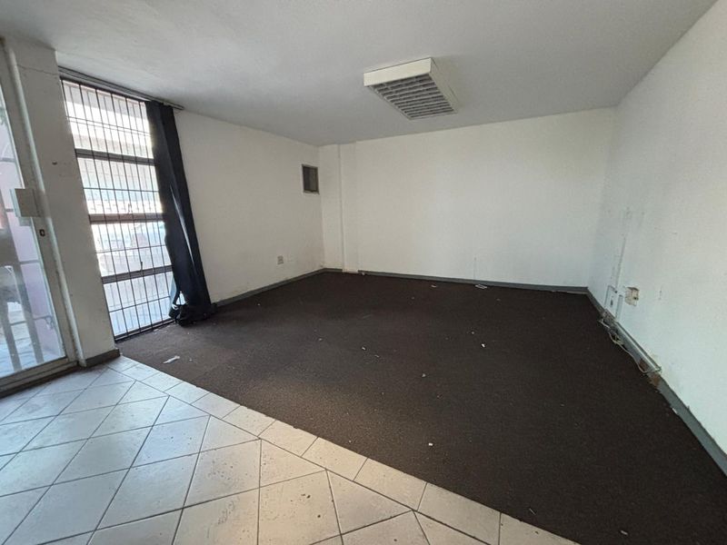 An empty office space featuring a mix of tiled and carpeted flooring, a fluorescent light fixture, and a security gate on the window.