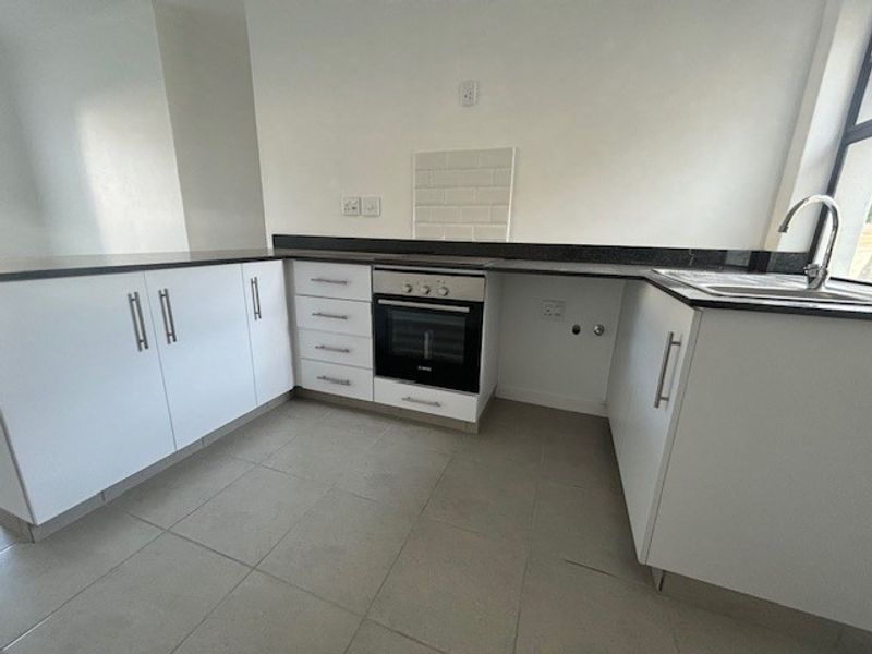 A clean, modern kitchen featuring white cabinetry, dark stone countertops, a built-in oven, and neutral tiled flooring.