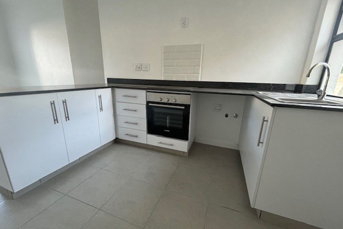 A clean, modern kitchen featuring white cabinetry, dark stone countertops, a built-in oven, and neutral tiled flooring.