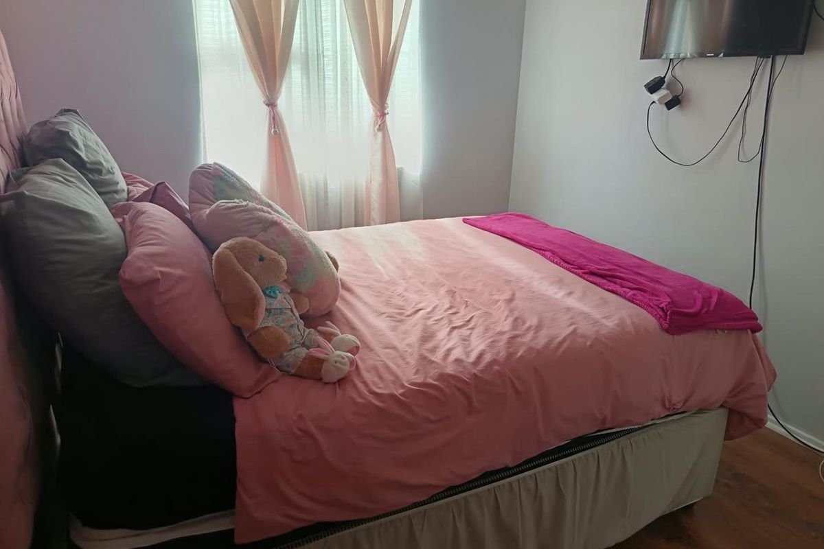 A standard bedroom featuring laminate flooring and a window with installed curtain rails, providing a functional sleeping space.