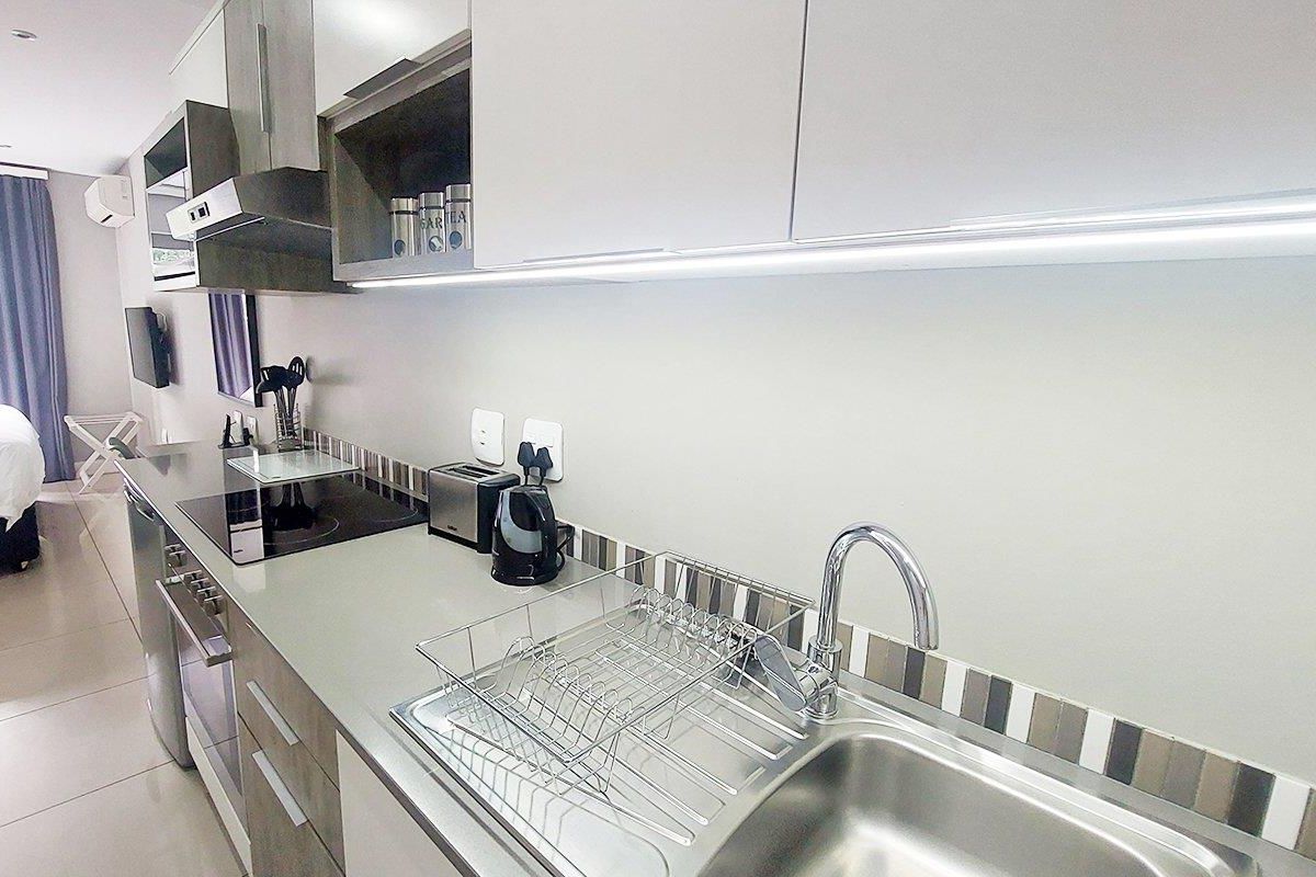 Modern galley-style kitchen featuring sleek cabinetry, integrated appliances, a stainless steel sink, and contemporary tiled backsplash with under-cabinet lighting.