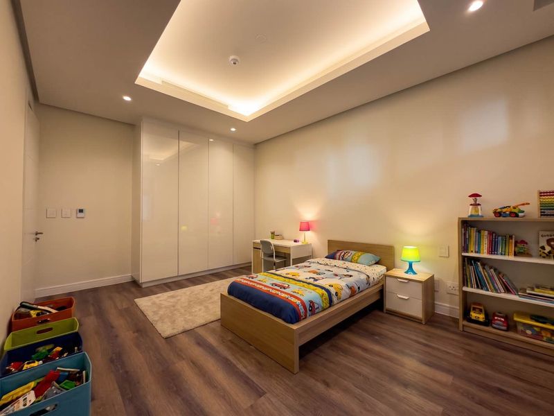 A well-maintained bedroom featuring modern laminate flooring, a large built-in wardrobe, and elegant recessed ceiling lighting.