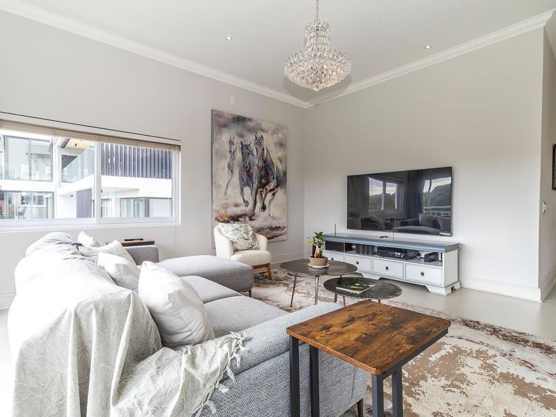 A bright and spacious living room featuring recessed lighting, a decorative chandelier, and large windows allowing for ample natural light.