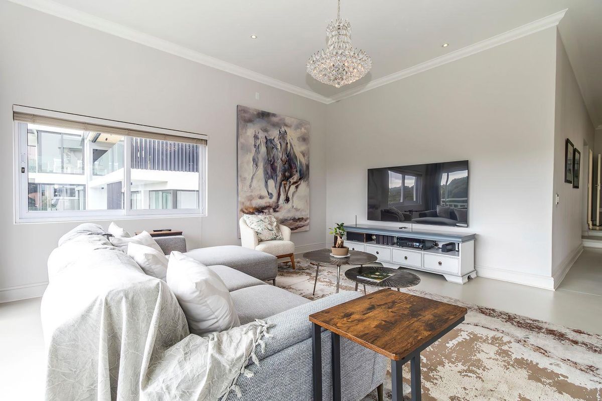 A bright and spacious living room featuring recessed lighting, a decorative chandelier, and large windows allowing for ample natural light.