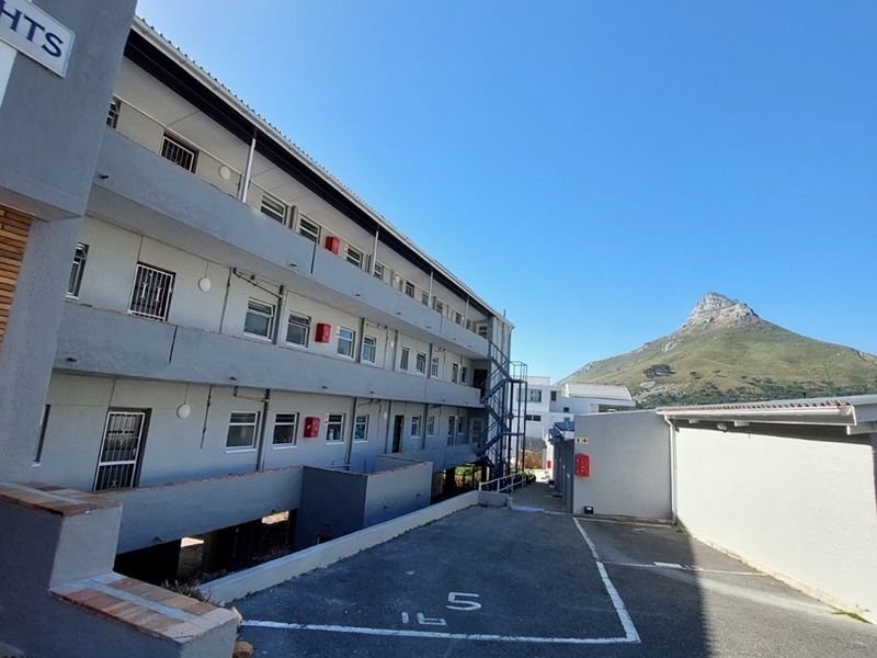 Exterior view of an apartment building facade featuring a paved parking area, metal fire escape, and mountain views.