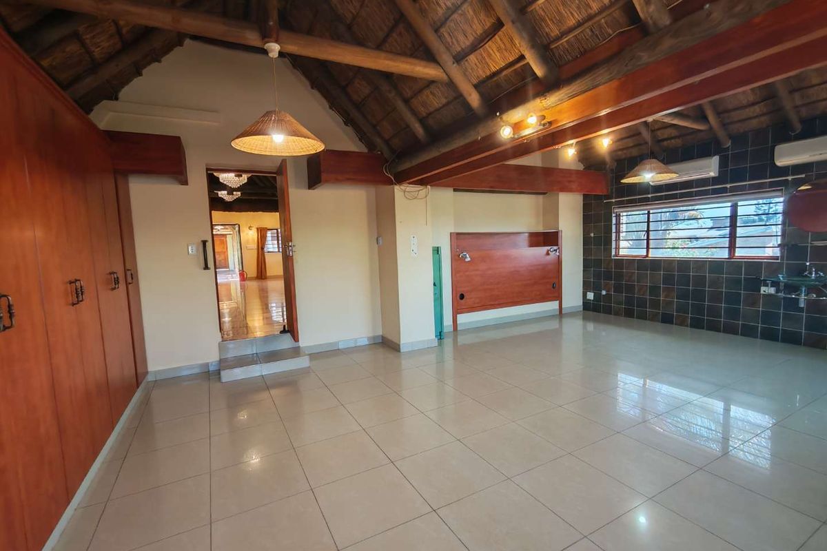 Spacious bedroom featuring a high thatched ceiling with exposed timber beams, tiled flooring, built-in cupboards, and an air conditioning unit.