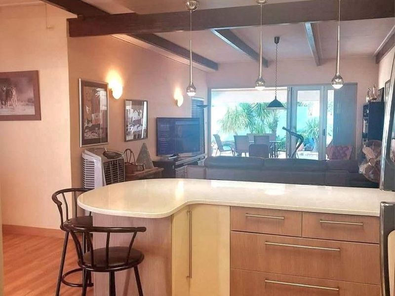 Open plan kitchen and living area featuring a central island with stone countertops, timber cabinetry, and exposed ceiling beams leading to an outdoor patio.