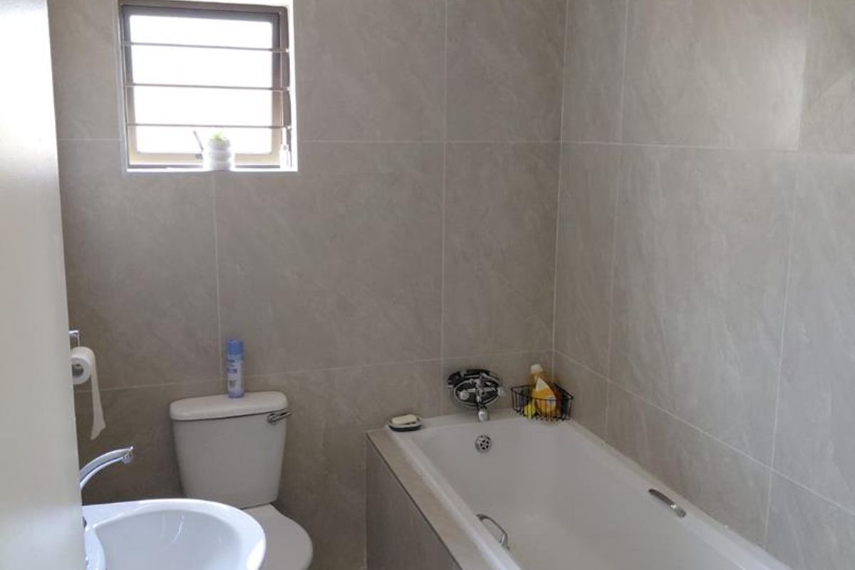 A clean, modern bathroom featuring floor-to-ceiling neutral wall tiles, a white pedestal basin, a toilet, and a built-in bathtub.