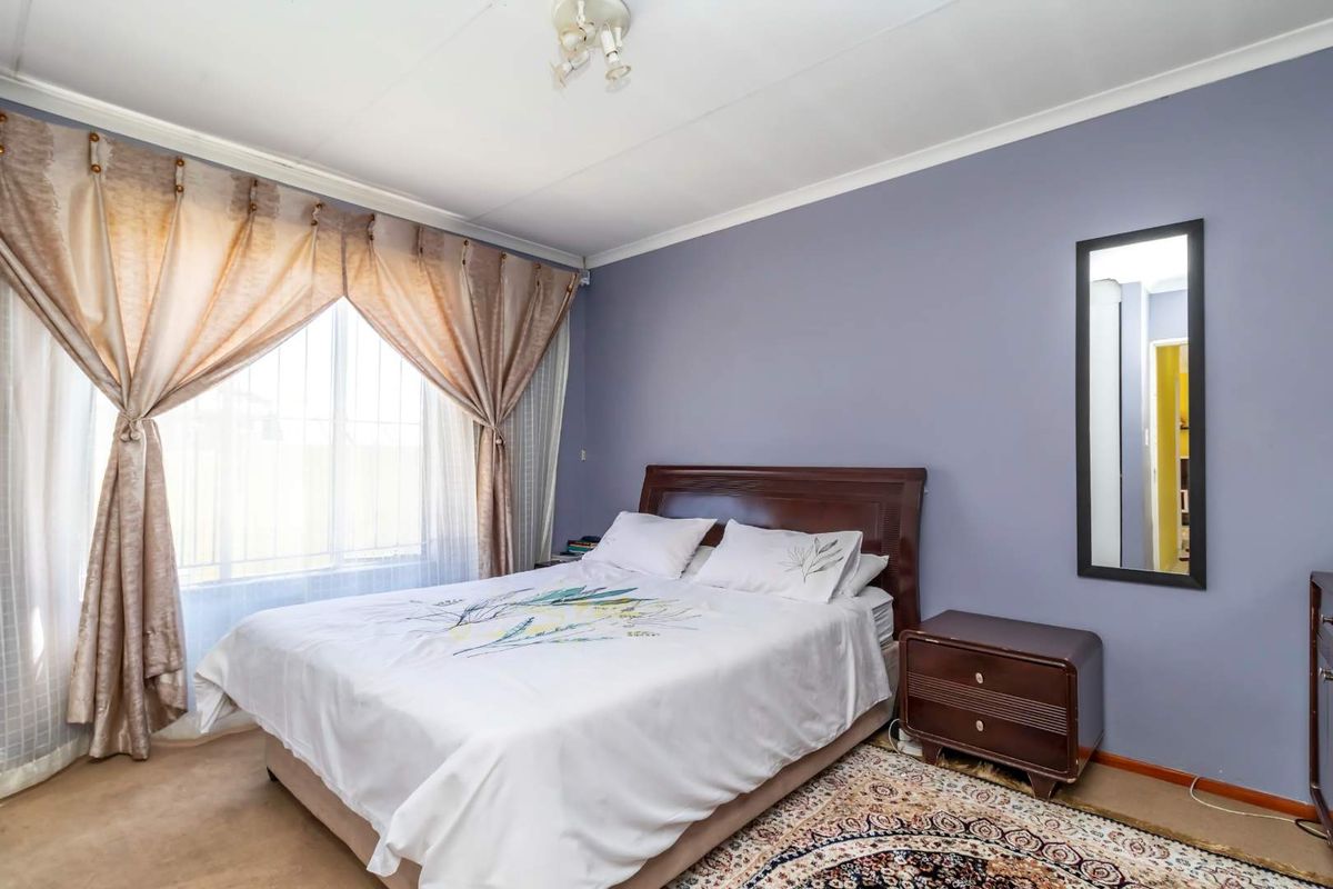 A standard bedroom featuring carpeted flooring, a large window with curtain fixtures, and neutral wall paint.