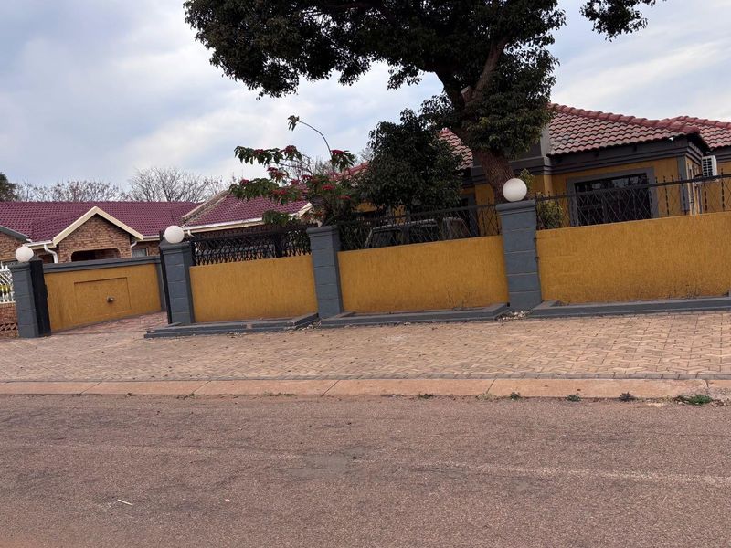 Front exterior view of a residential house featuring a paved driveway, perimeter wall with pillar lighting, and a tiled roof.