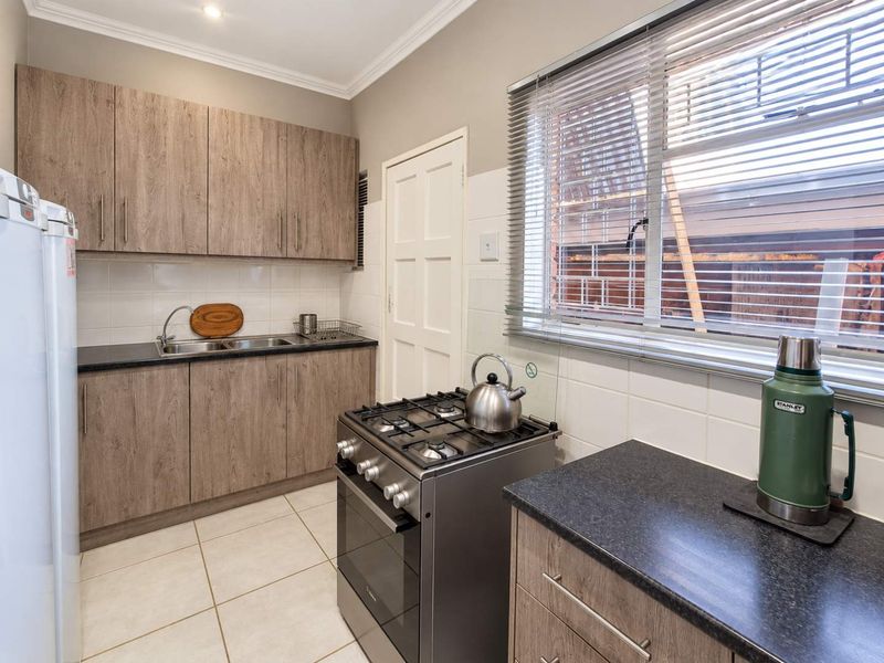 A functional kitchen featuring wood-look cabinetry, dark countertops, a gas stove, and tiled flooring, offering a clean and practical workspace.