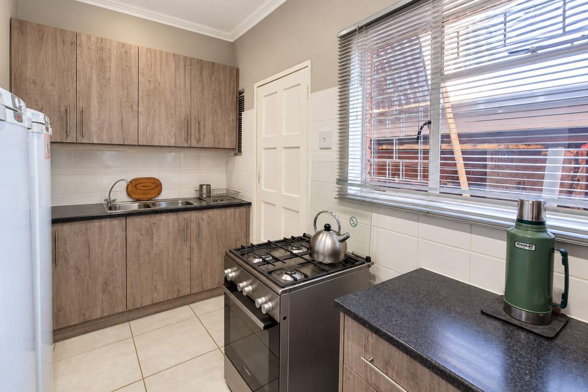 A functional kitchen featuring wood-look cabinetry, dark countertops, a gas stove, and tiled flooring, offering a clean and practical workspace.