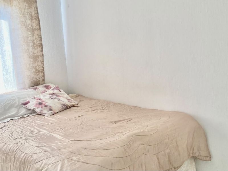 A simple bedroom space featuring plain white walls and a window with curtains.