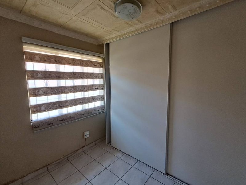 A compact bedroom featuring tiled flooring, a built-in sliding door wardrobe, and a window with a roller blind.