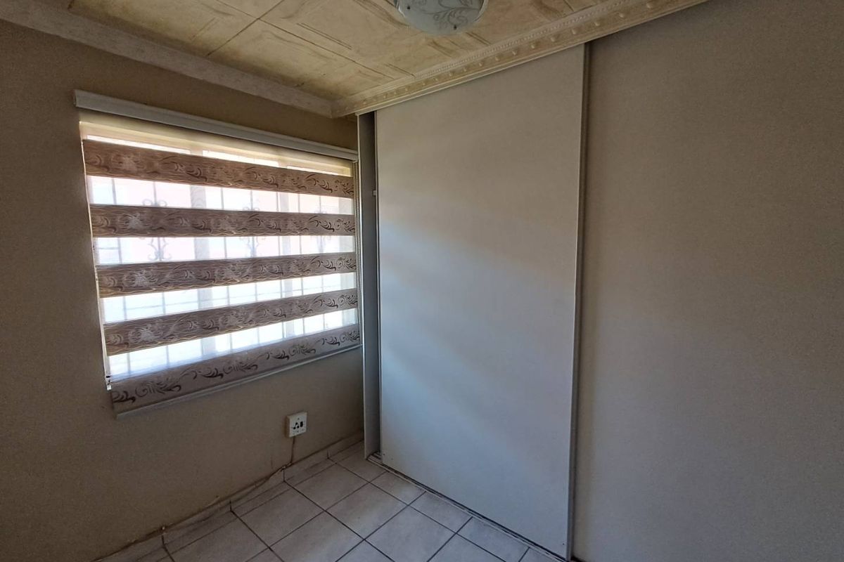 A compact bedroom featuring tiled flooring, a built-in sliding door wardrobe, and a window with a roller blind.