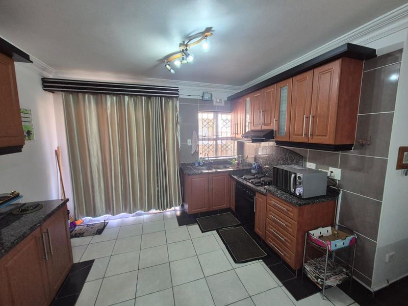 A functional kitchen featuring wooden cabinetry, granite countertops, built-in oven, gas hob, and tiled flooring with direct access to a patio area.