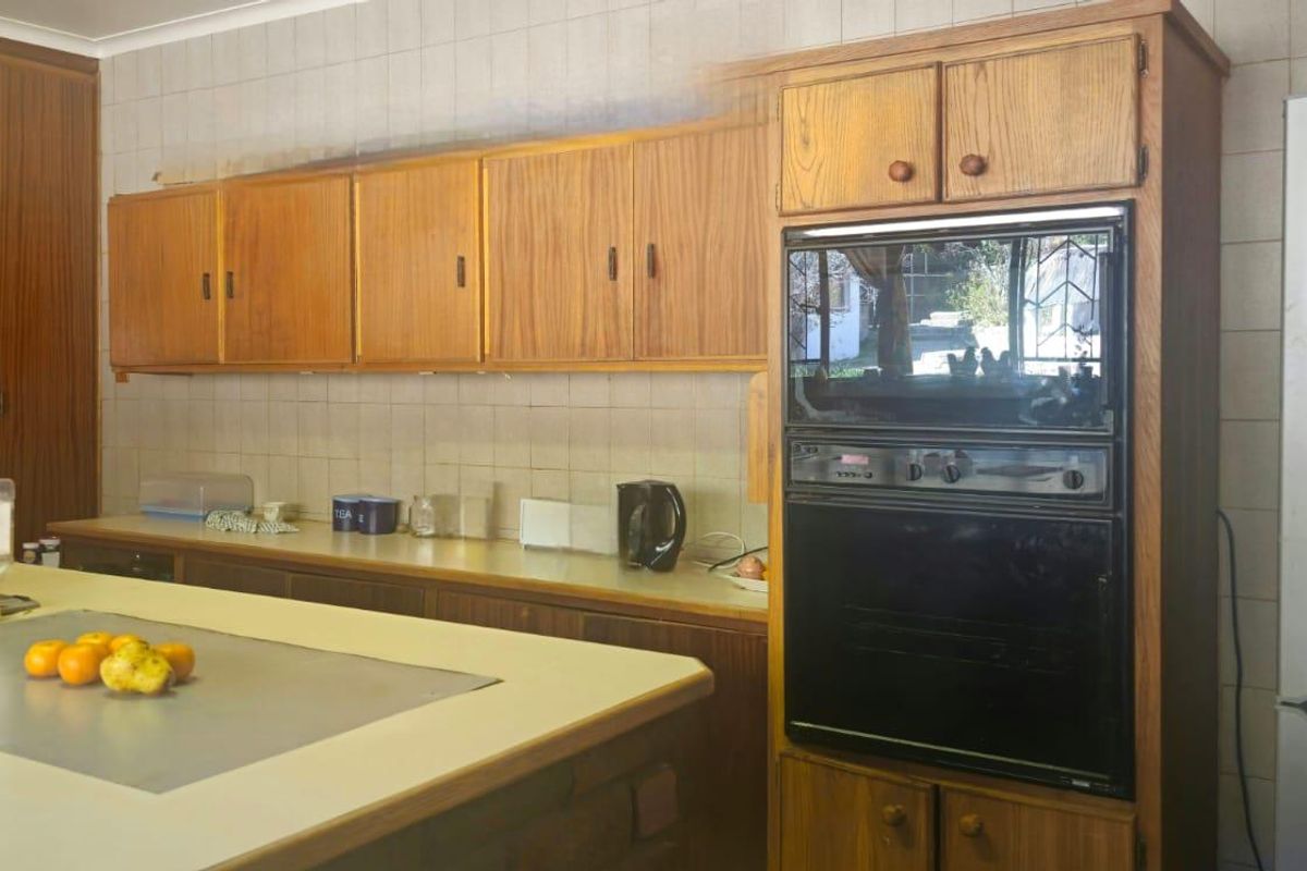 A dated kitchen featuring wood-veneer cabinetry, tiled splashbacks, and a built-in eye-level oven, offering a functional layout with potential for modern renovation.