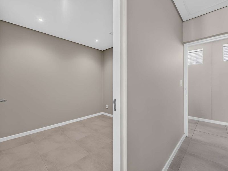 A clean, neutral-toned hallway featuring modern tiled flooring and recessed downlighting, providing a bright and seamless transition between interior spaces.