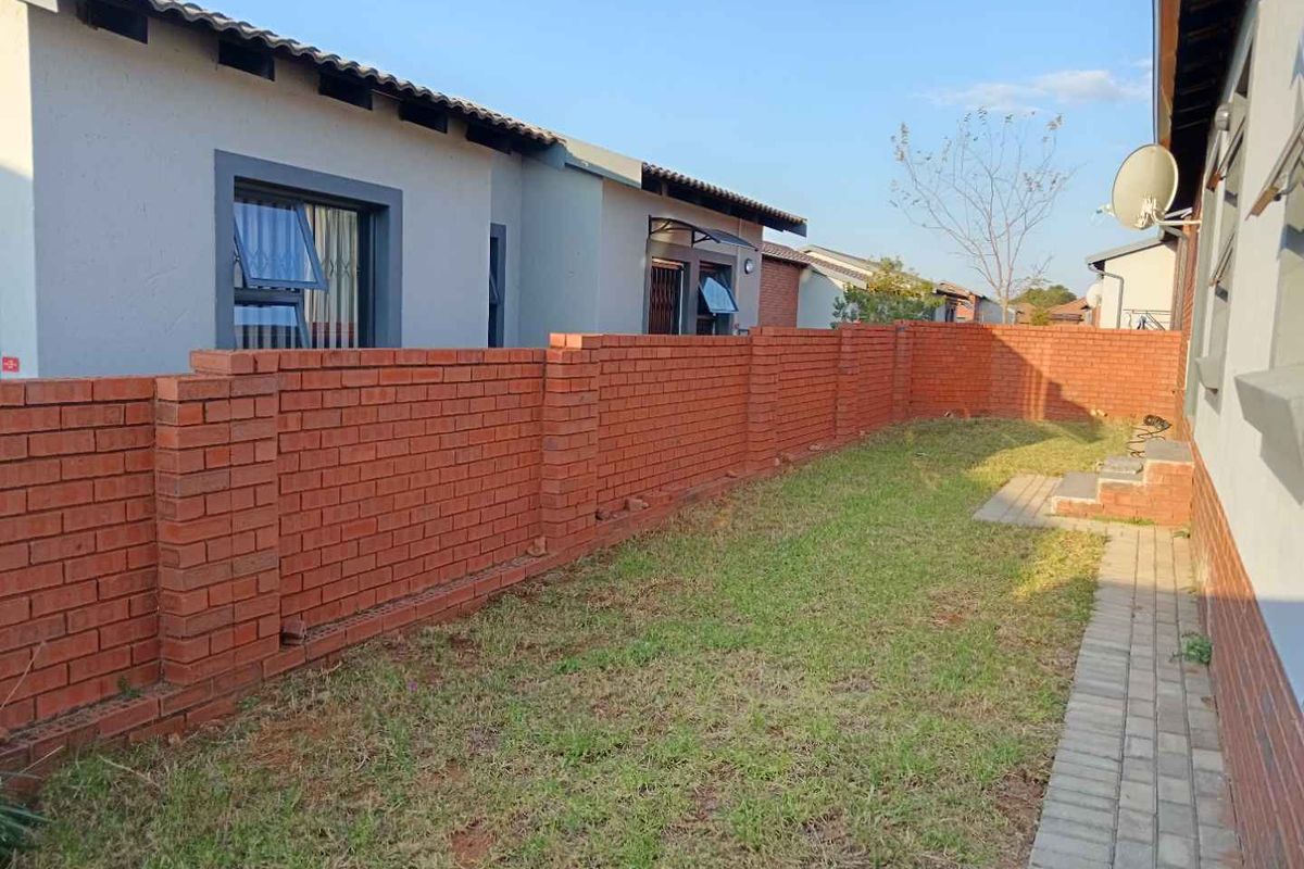 A private rear garden area featuring a red brick boundary wall, paved walkway, and lawn space adjacent to the townhouse structure.