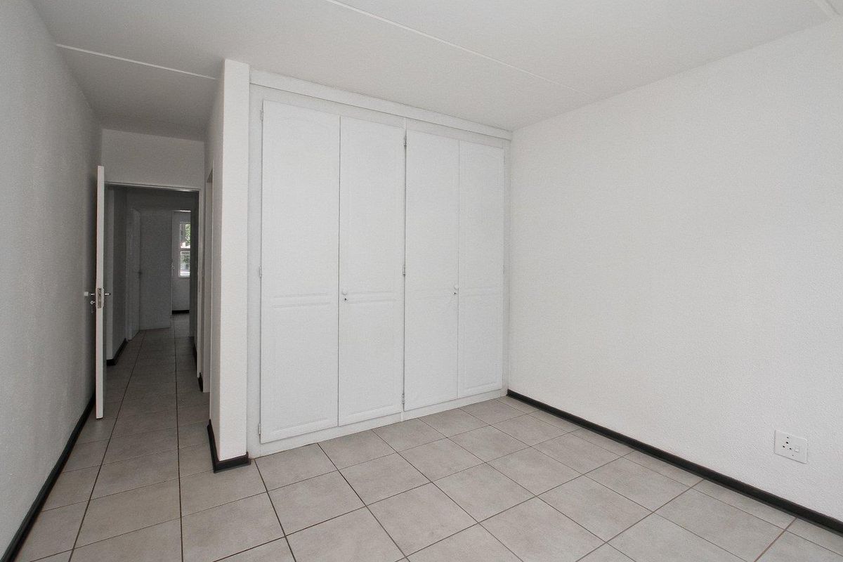 A clean, empty bedroom featuring neutral tiled flooring and ample built-in cupboard storage, leading into a hallway.