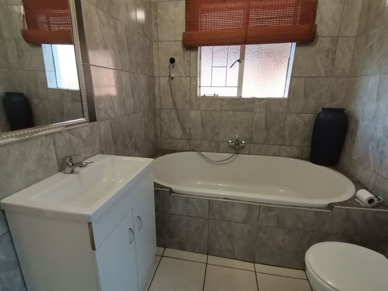 A functional bathroom featuring a built-in vanity, a bathtub with a handheld shower mixer, and neutral wall and floor tiling.