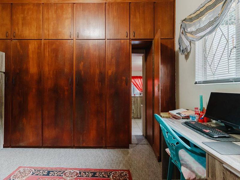 Bedroom featuring extensive floor-to-ceiling wooden built-in cupboards, a window with security bars, and venetian blinds.